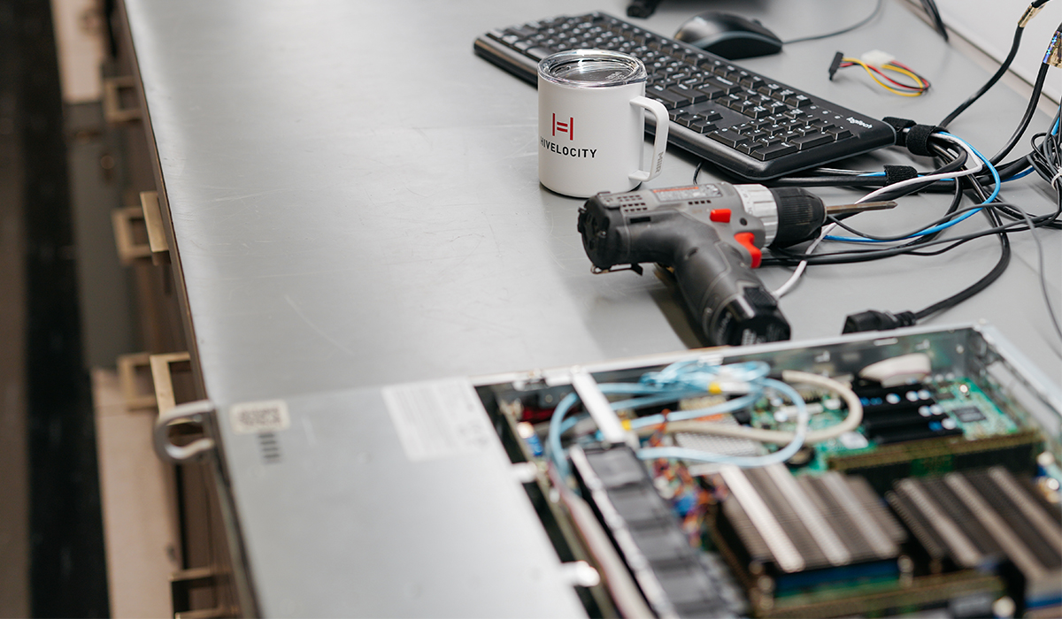 A opened server sitting on a table next to a power drill and coffee mug with the Hivelocity logo