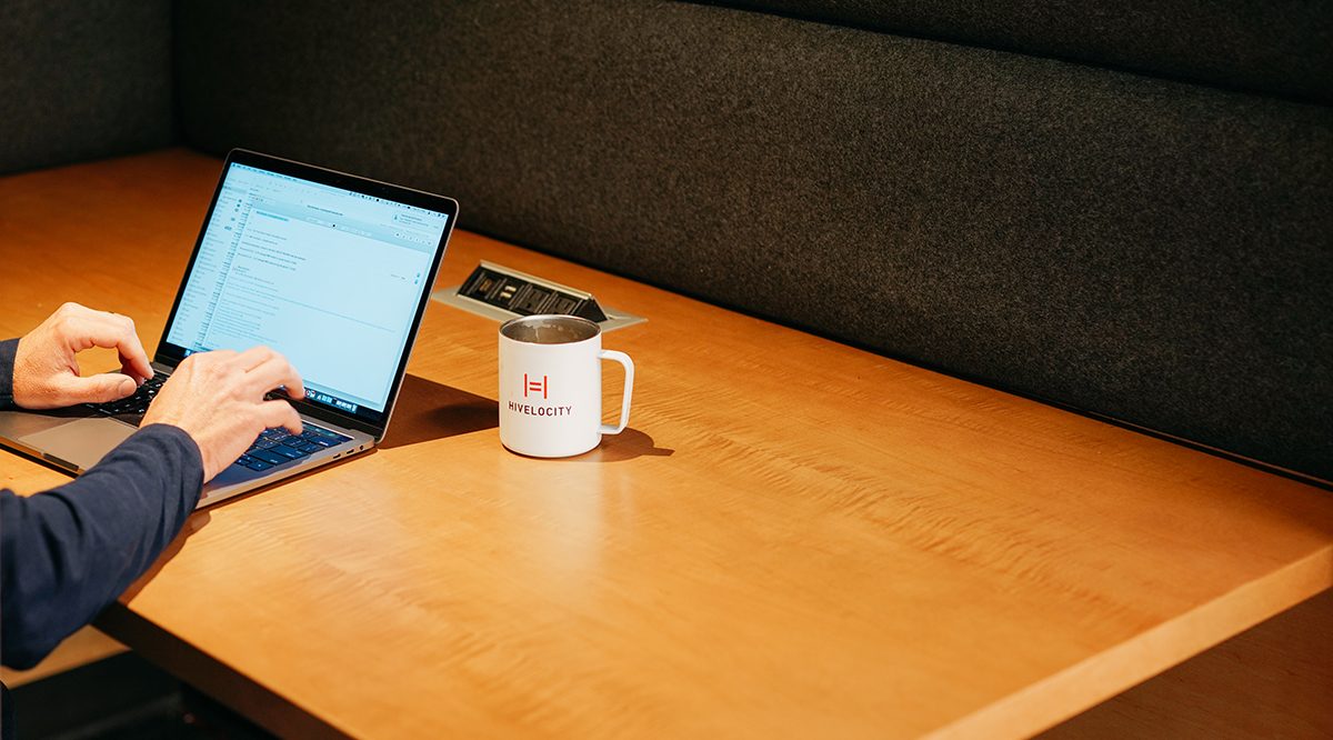 Hands working on a laptop next to a coffee mug with the Hivelocity logo on it